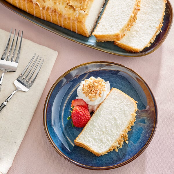 A slice of coconut-flavored pound cake served with whipped cream, toasted coconut, and a strawberry on a blue plate.