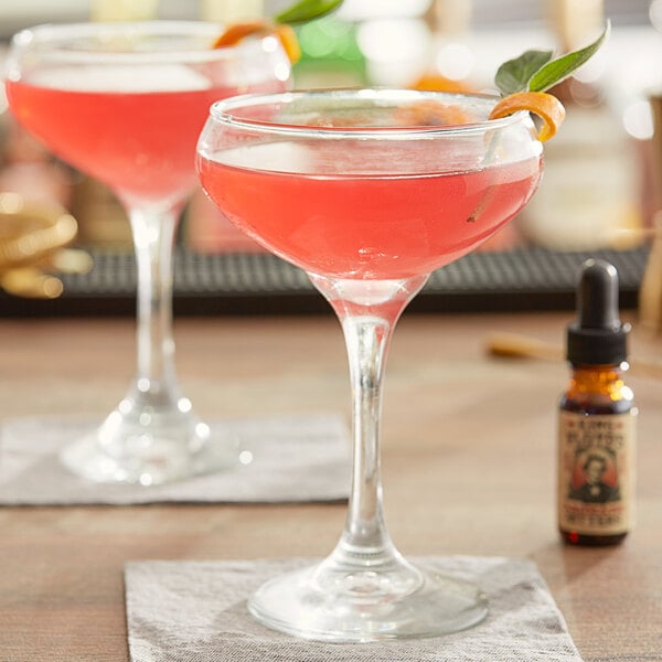 Two glasses of King Floyd's pink cocktails with orange garnish on a table.