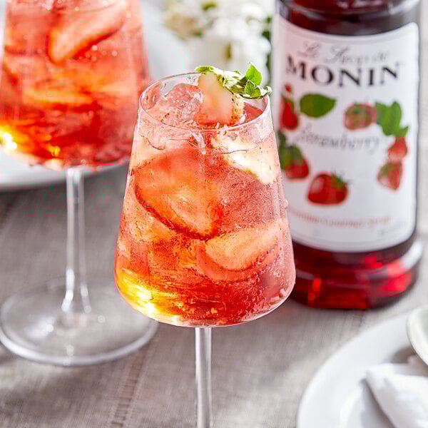 A glass of red liquid with a straw and mint leaves on the rim.