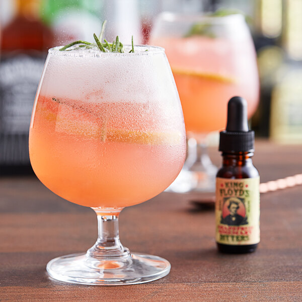 A glass of pink liquid with a dropper next to it and a bottle of King Floyd's Grapefruit Rosemary Bitters.