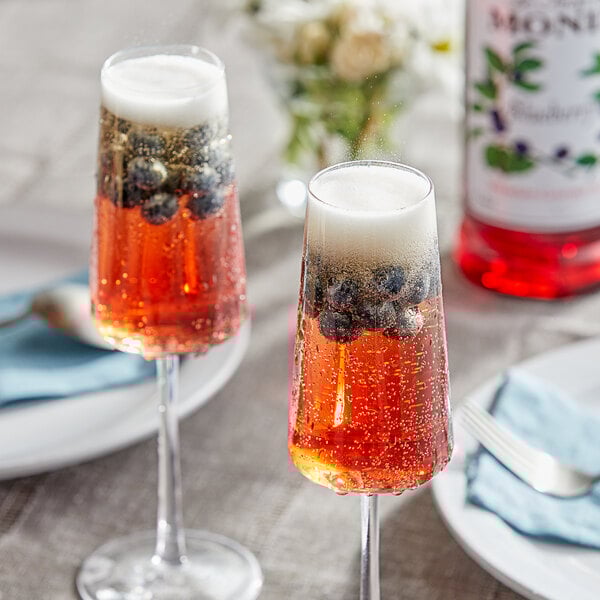 Two glasses of red liquid with Monin Blueberry syrup and blueberries.