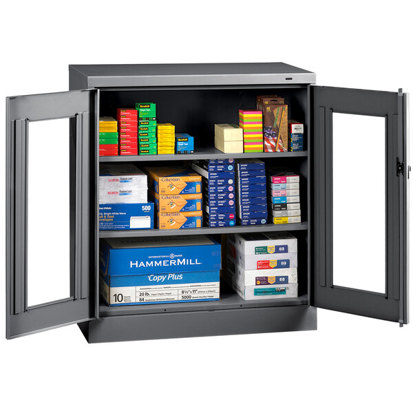 A dark gray Tennsco metal storage cabinet with C-Thru doors holding boxes and papers.