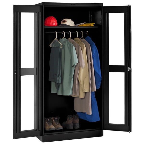 A black Tennsco wardrobe cabinet with clear doors filled with clothes.