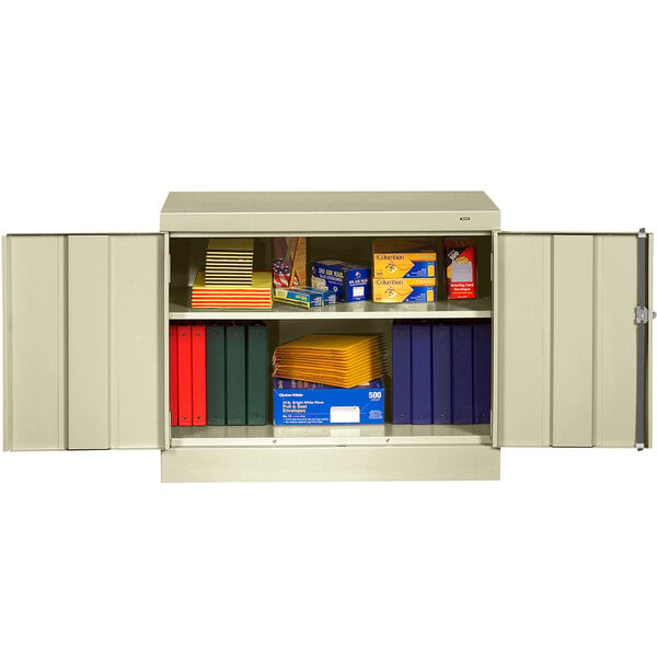 A putty metal Tennsco storage cabinet with books and boxes inside.