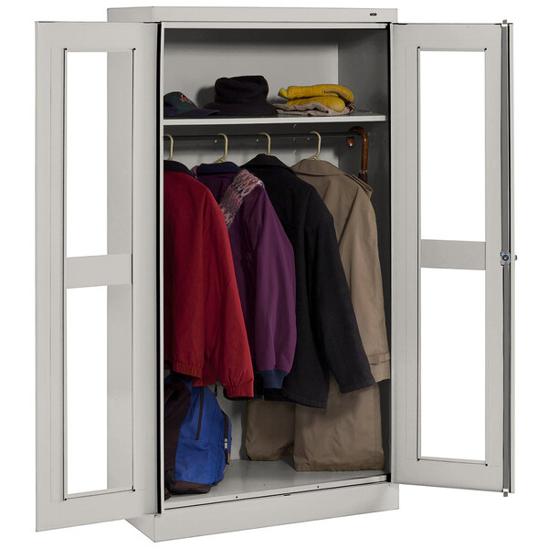 A light gray Tennsco wardrobe cabinet with C-Thru doors holding clothes.
