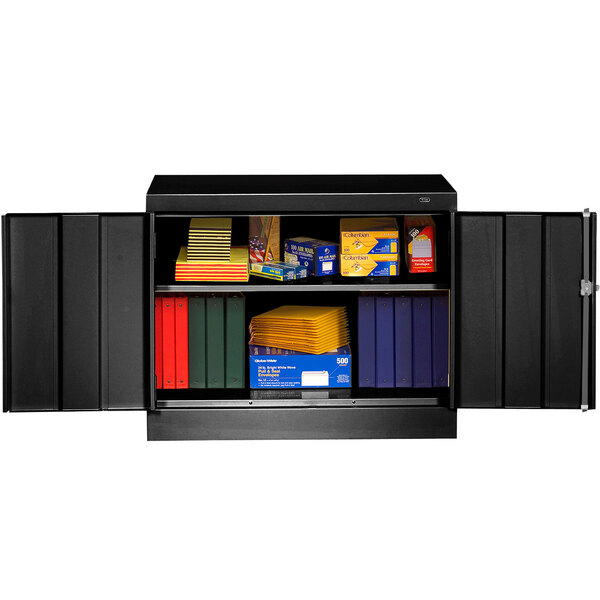 A black metal Tennsco storage cabinet with solid doors and shelves full of books and boxes.
