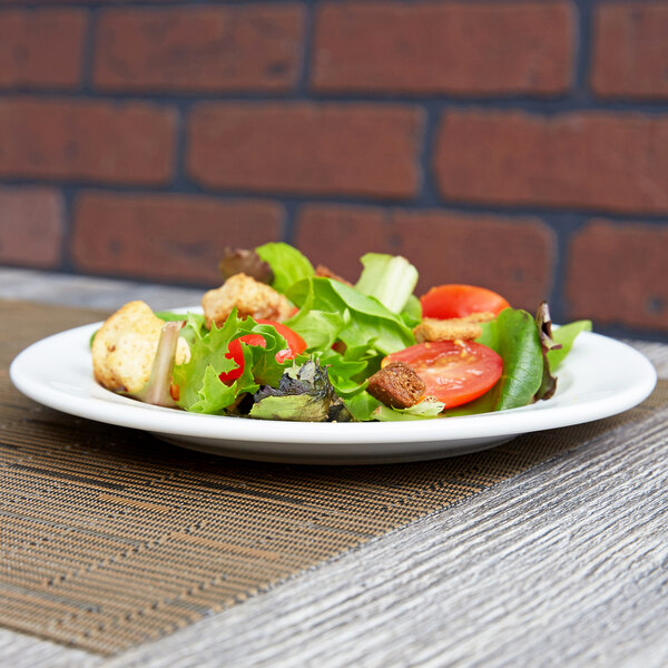 An Arcoroc white porcelain side plate with salad on a table.
