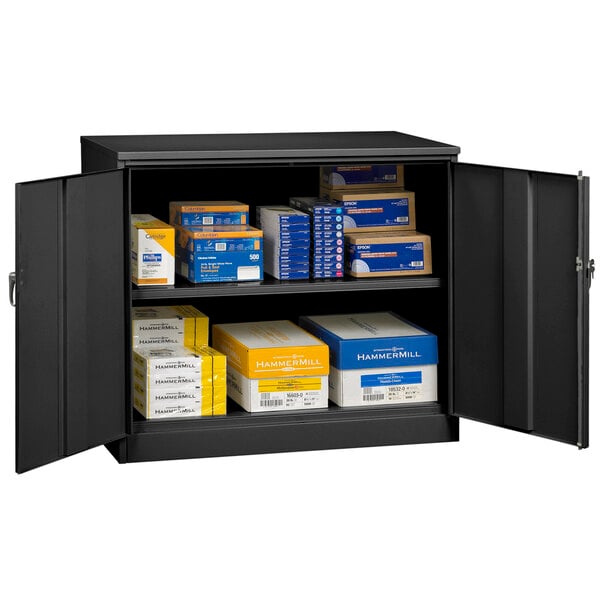 A black metal Tennsco jumbo storage cabinet with solid doors and shelves full of boxes.