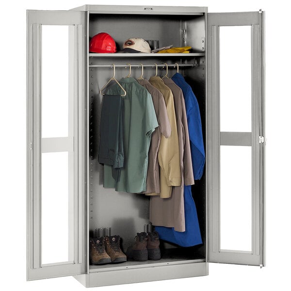 A light gray metal Tennsco deluxe wardrobe cabinet with clothes and shoes behind c-thru doors.