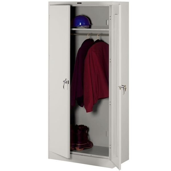 A light gray metal Tennsco wardrobe cabinet with solid doors holding a red shirt and a helmet.