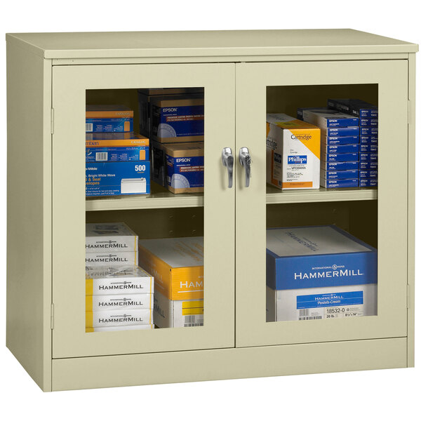 A Tennsco putty jumbo storage cabinet with C-thru doors with a few boxes on it.