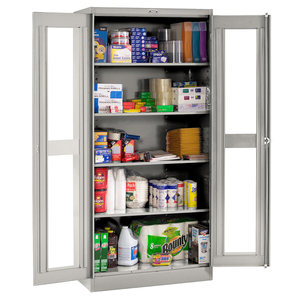 A light gray Tennsco metal storage cabinet with C-Thru doors and shelves full of a variety of products.
