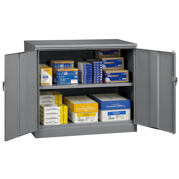 A dark gray Tennsco metal storage cabinet with solid doors holding many boxes.