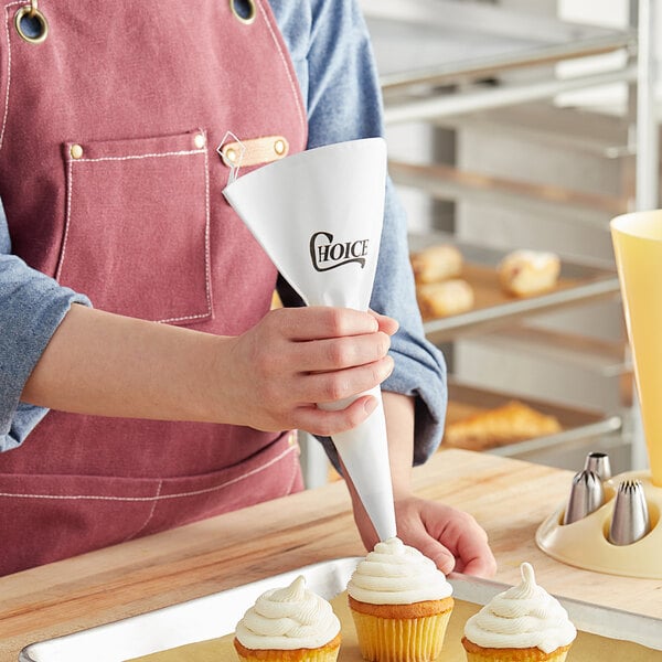 A person using a Choice plastic coated canvas pastry bag to frost cupcakes.