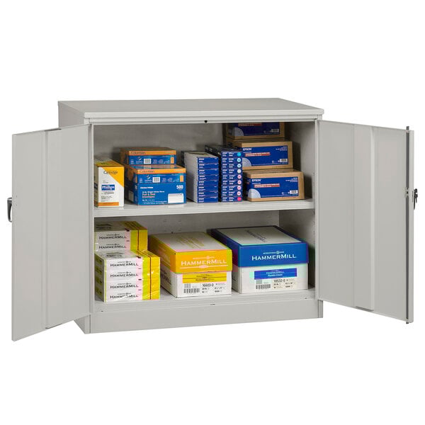 A light gray Tennsco industrial storage cabinet with solid doors and many boxes inside.
