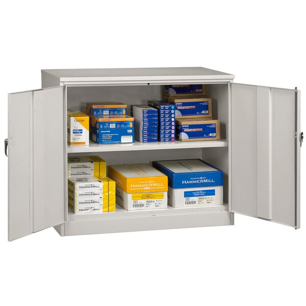 A light gray Tennsco metal storage cabinet with solid doors and many boxes inside.