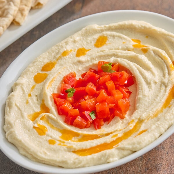A bowl of hummus topped with diced red bell peppers and a drizzle of oil.