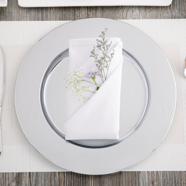 A silver Carlisle charger plate with a napkin and flowers on it.