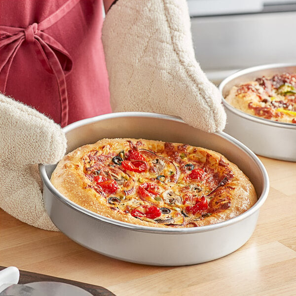 A person holding a deep dish pizza in a Choice aluminum pizza pan.