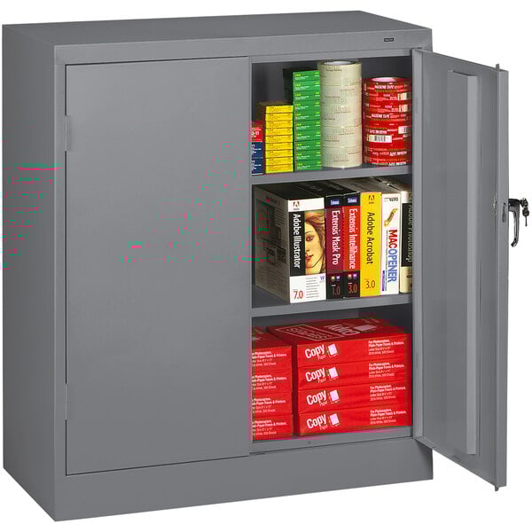 A dark gray Tennsco storage cabinet with solid doors filled with books and cans.