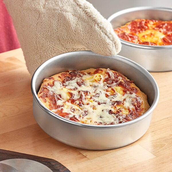A person wearing a glove holding a deep dish pizza in a Choice aluminum pan.