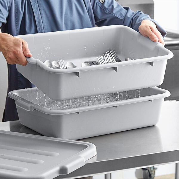 A man holding a Choice gray polypropylene drain box and flatware soaker container full of silverware.