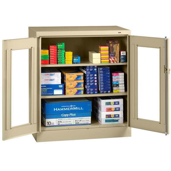 An unassembled sand Tennsco storage cabinet with C-Thru doors open to reveal many boxes.