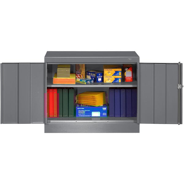 A metal Tennsco dark gray storage cabinet with books and folders.