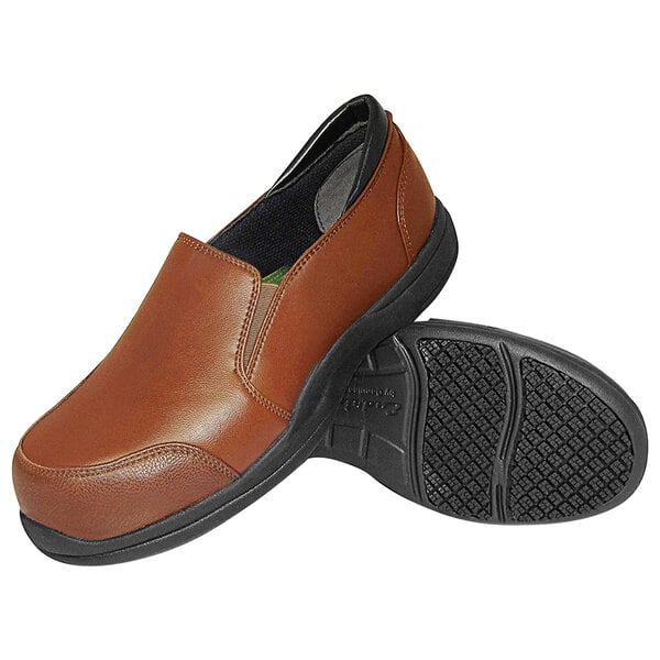 A pair of brown slip-on shoes with black non-slip soles, one shoe shown upright and the other displaying the tread pattern.