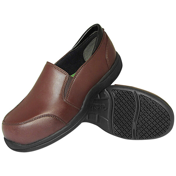 A pair of brown slip-on shoes with black non-slip soles, one shoe shown upright and the other displaying the tread pattern.