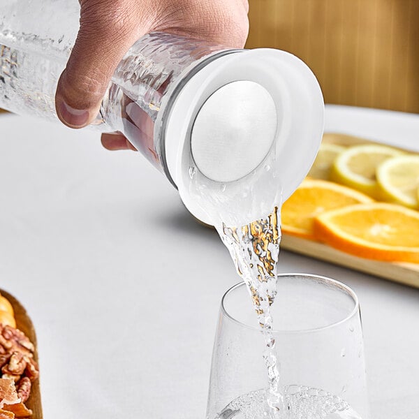 A hand using a Front of the House Drinkwise self pour carafe lid to pour water into a glass.