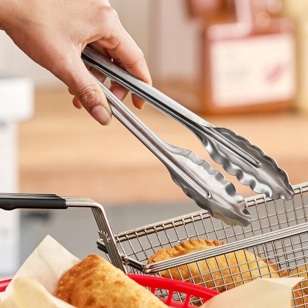 A pair of heavy-duty stainless steel utility tongs being used in a kitchen setting.