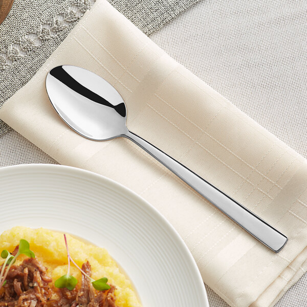 An Acopa stainless steel dinner spoon on a white napkin.