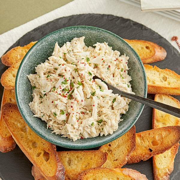 A bowl of crab dip with a spoon on a plate.