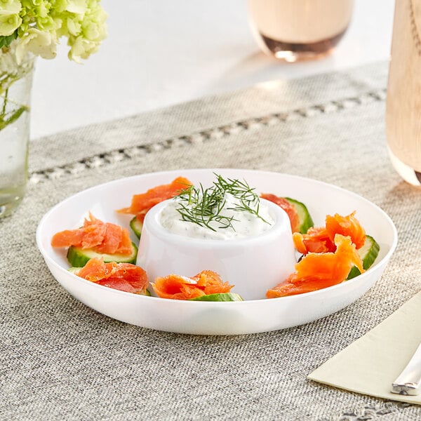 A white plastic mini circular dip tray with salmon and cream on it with green sprigs of dill.