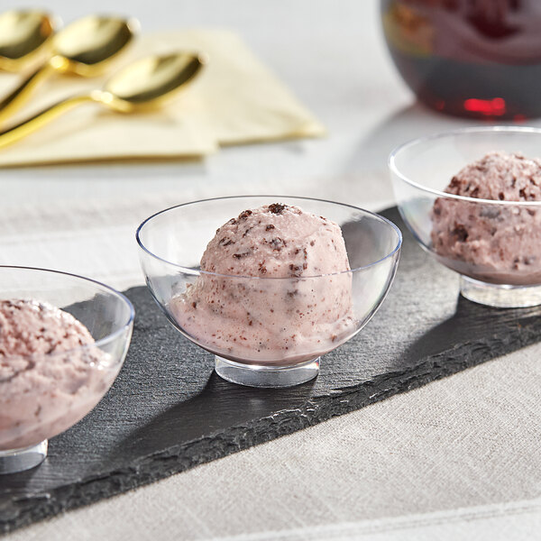 Three clear plastic mini bowls filled with ice cream topped with chocolate sauce.