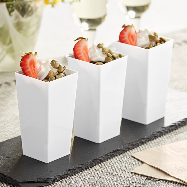 A group of white Choice square plastic mini cups with strawberries and nuts inside.