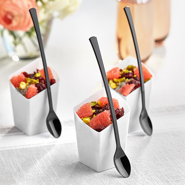 White containers of fruit with black Visions tasting spoons.