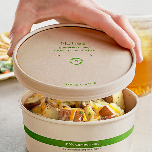 A hand holding a World Centric compostable container of food.