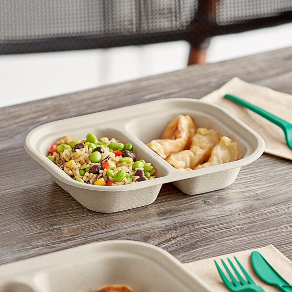 A World Centric compostable fiber container with two compartments of food on a table with a green fork.