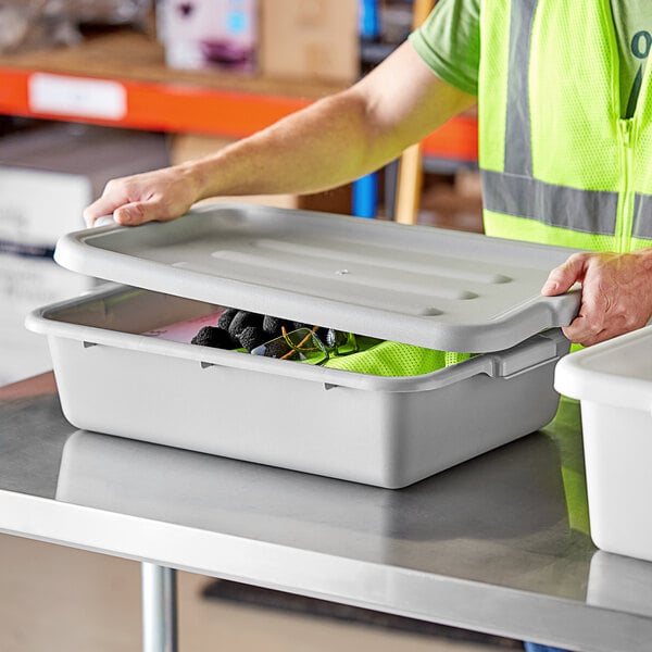 A man in a safety vest opening a Lavex gray plastic utility bin with a lid.