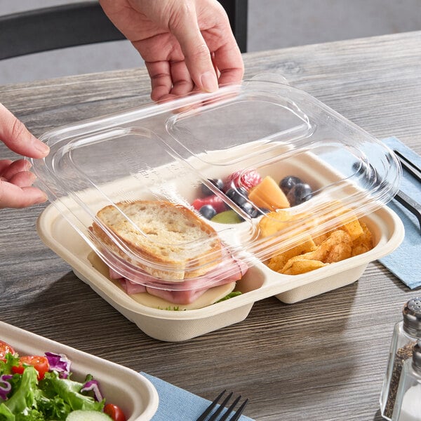 A clear compostable three-compartment PLA lid being placed on a divided food container.