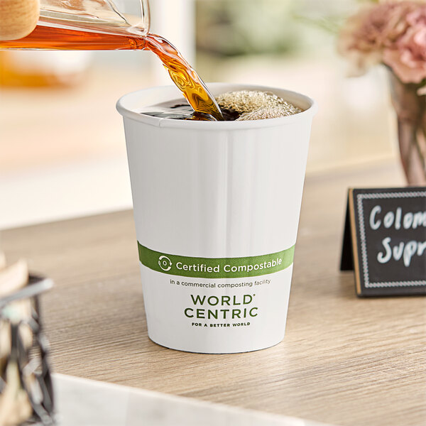 A cup of coffee being poured into a white World Centric compostable paper hot cup.