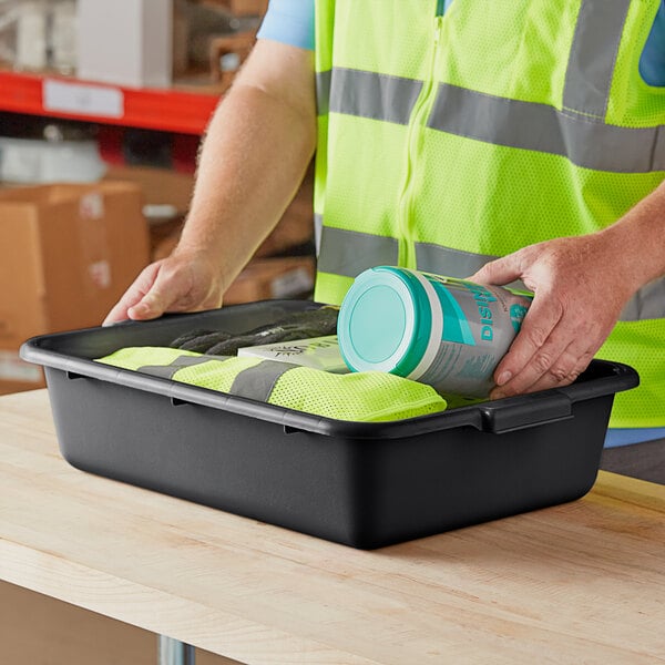 A person in a reflective vest using a Lavex black utility bin to pack food.