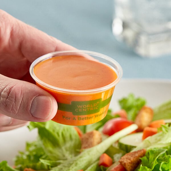 A hand holding a World Centric compostable portion cup of food.