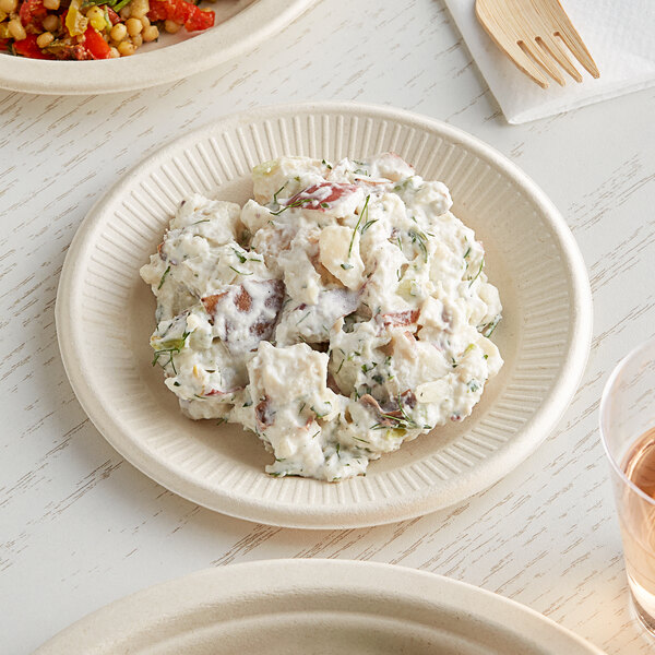 A World Centric compostable fiber plate with potato salad, a wooden fork, and a glass of wine on a table.
