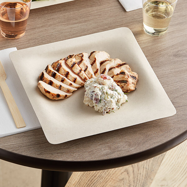 A World Centric compostable fiber plate with chicken and potato salad on a table.