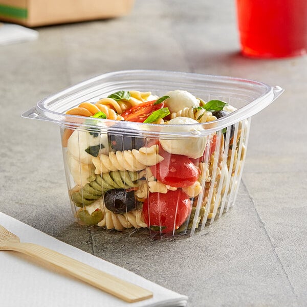 A World Centric clear plastic deli container of pasta and vegetables with a wooden fork 