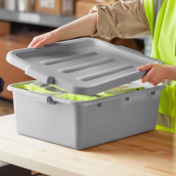 A person in a yellow vest opening a Lavex gray polypropylene utility lid on a plastic container.