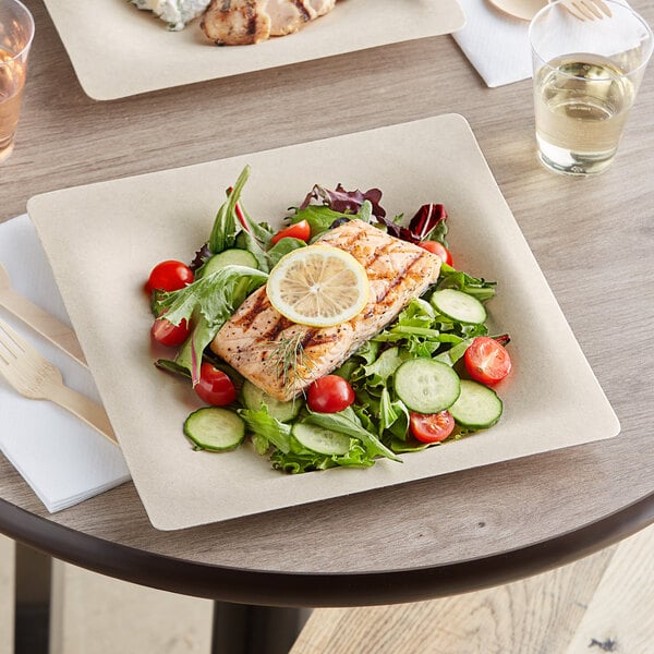 A World Centric compostable fiber plate with a salad and salmon on a table with a wooden fork and knife.